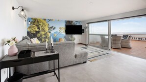 A modern living room with a grey sofa, a black side table, a pink vase, and a flat-screen TV. - Apartment "Casa Hola Mar" Directly on the Coast with Infinity Sea View (Los Realejos)