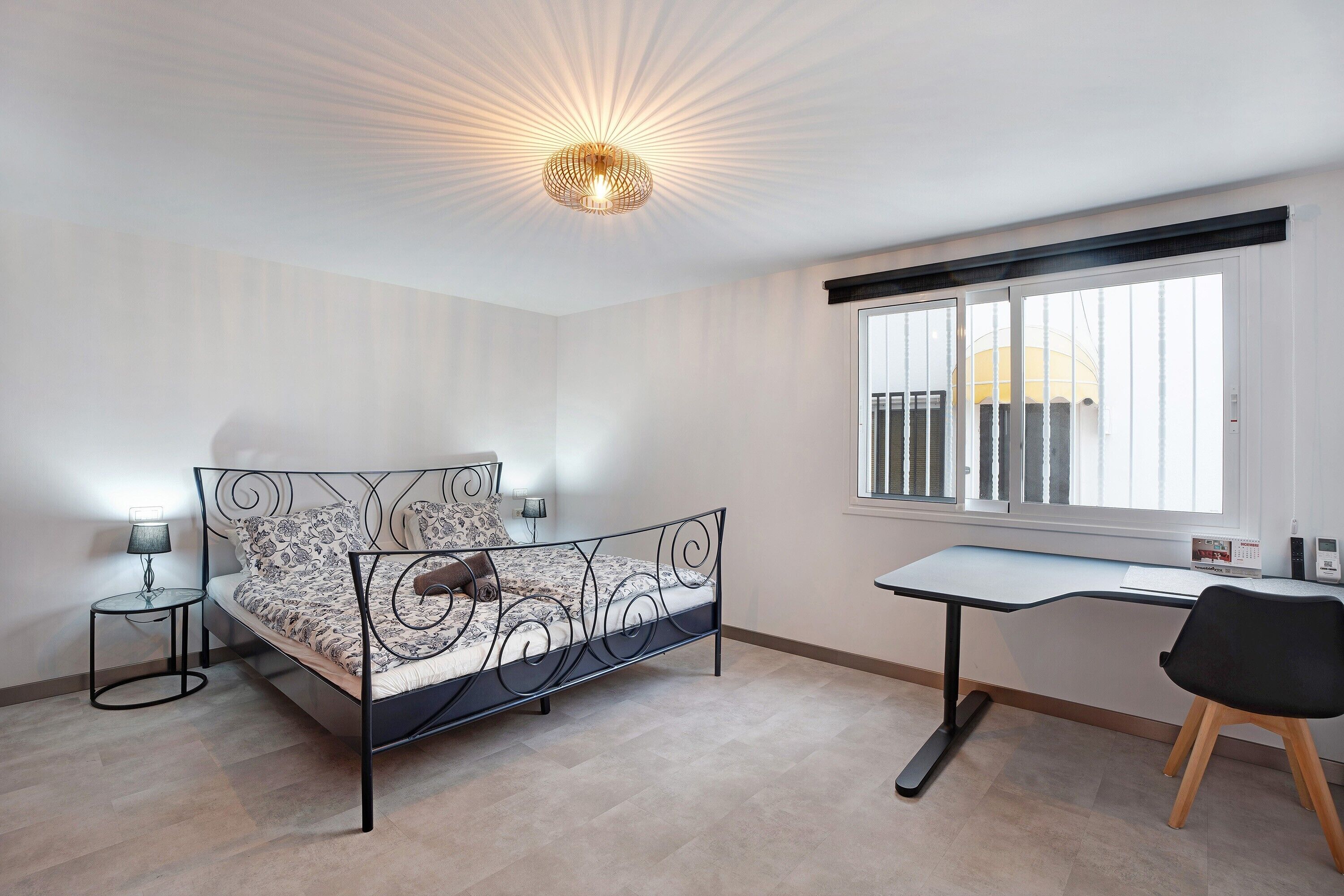Een slaapkamer met een bed, nachtkastjes, een bureau, een stoel, een raam met uitzicht en een plafondlamp.