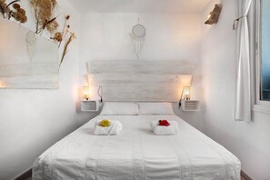 A bedroom with a large bed, two bedside tables, a wall-mounted dreamcatcher, and a window with curtains.