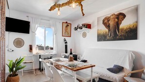 A dining area with a wooden table, white chairs, a white sofa, and a large elephant painting on the wall. - Apartment "Casa Chipiron" with Mountain View, Terrace & Wi-Fi (Vejer de la Frontera)