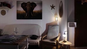 A room with a bed, a dining table set for two, a chair, a small table with a lamp, and a wall with a framed picture of an elephant. - Apartment "Casa Chipiron" with Mountain View, Terrace & Wi-Fi (Vejer de la Frontera)