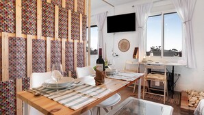 A dining area with a wooden table set for two, a TV mounted on the wall, and a window with curtains. - Apartment "Casa Chipiron" with Mountain View, Terrace & Wi-Fi (Vejer de la Frontera)