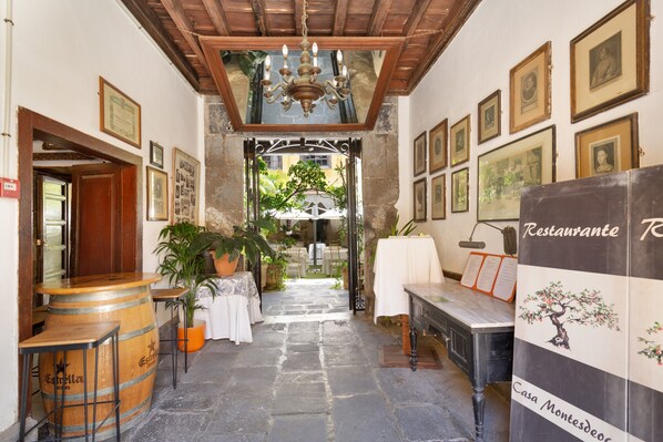 A corridor with stone flooring, wooden furniture, and framed pictures on the walls.