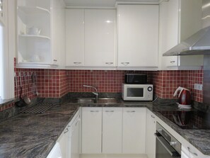 A kitchen with white cabinets, a microwave, a kettle, and a sink.