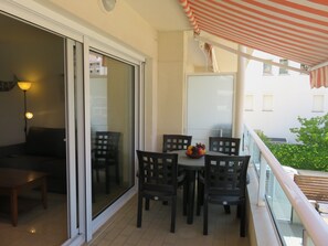 A balcony with a table, chairs, a bowl of fruit, and a striped awning. - Apartment "Brises del Mar 1-1" close to the Sea with Shared Pool & Wi-Fi (Girona)