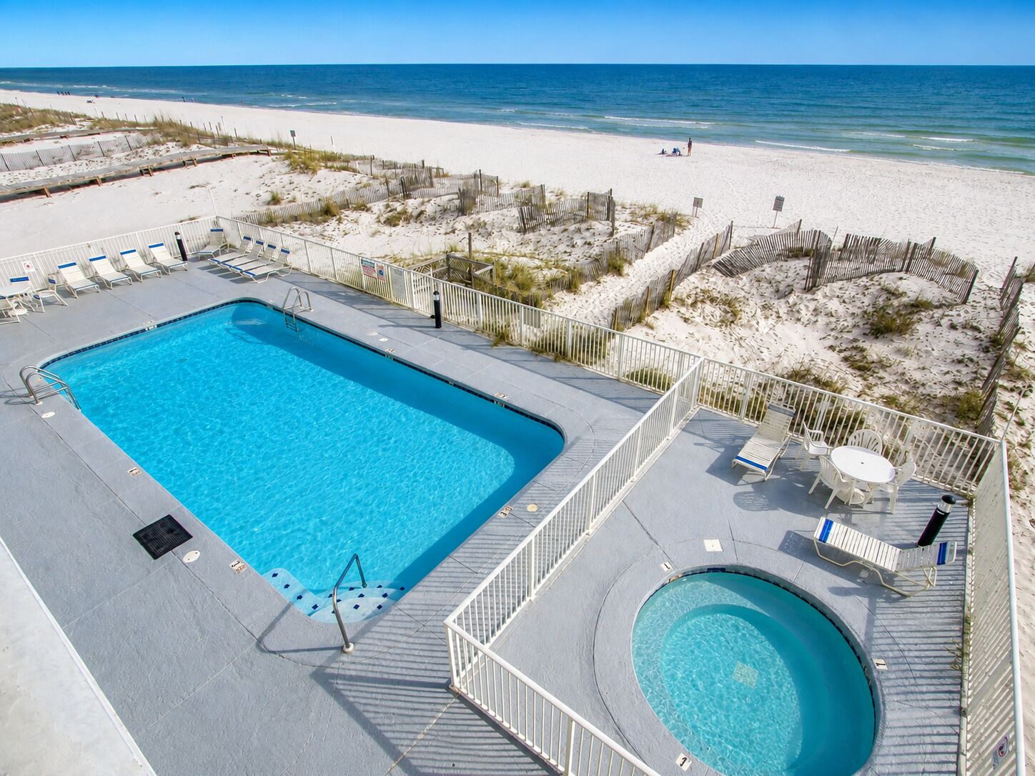 A swimming pool with a deck, surrounded by a sandy beach and ocean view.