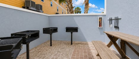 An outdoor patio with a grill, two barbecue smokers, a wooden bench, and a wall-mounted knife rack.