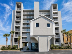 A multi-story building with balconies, a central entrance, and palm trees. - Shoreline Towers (Gulf Shores)