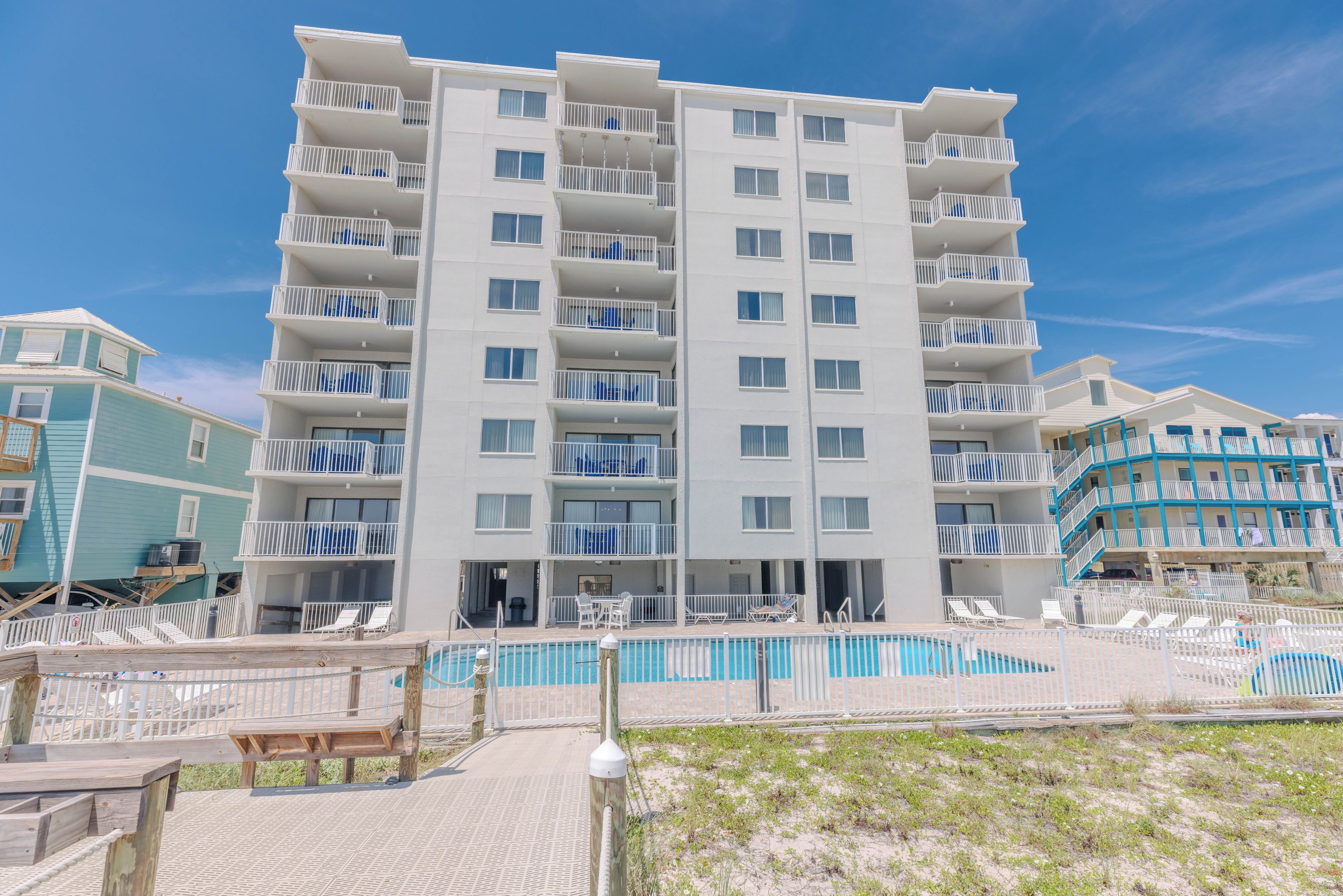 A multi-story hotel with balconies, a pool area, and a beach access walkway.