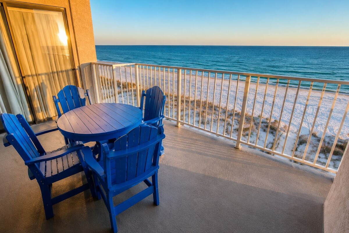 A balcony with a table and chairs overlooking a beach.