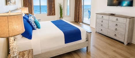 Une chambre à coucher avec un lit, une commode, un téléviseur et une vue sur l’océan.