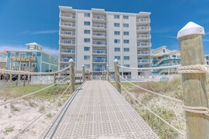 A beachside boardwalk leading to a multi-story hotel with balconies and a pool. - Shoreline Towers (Gulf Shores)