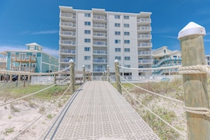 A beachside boardwalk leading to a multi-story hotel with balconies and a pool.