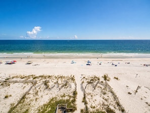 A beach with a wooden boardwalk leading to a beachside area with umbrellas and beach chairs. - Shoreline Towers (Gulf Shores)