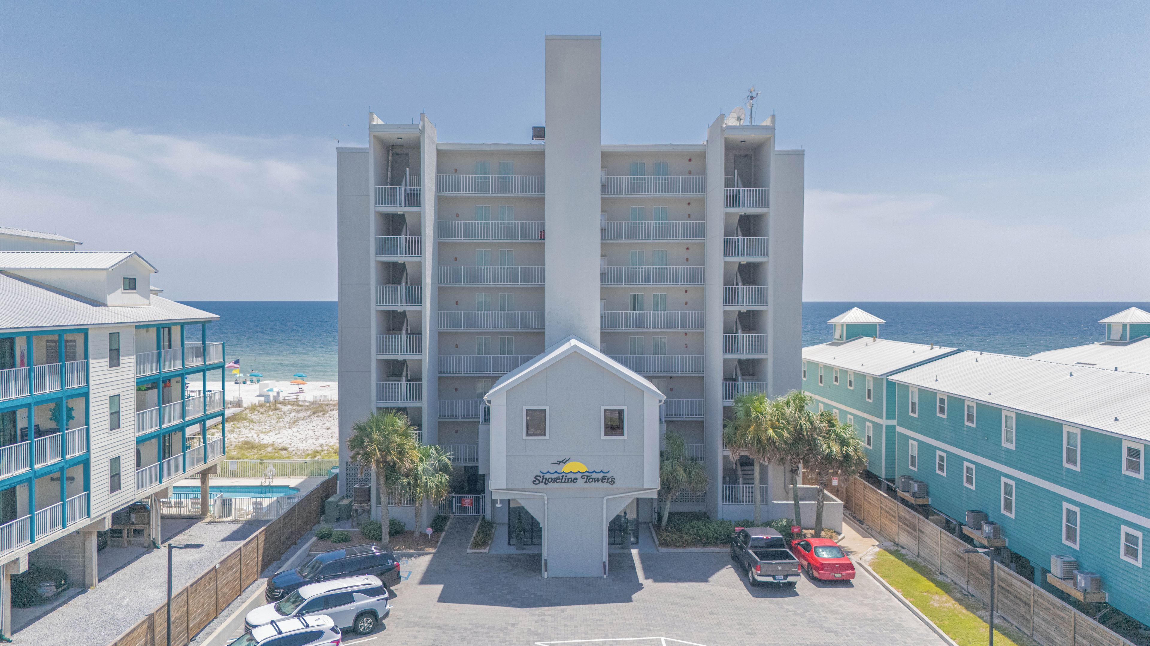 Un hôtel situé en bord de mer, avec un bâtiment principal, de nombreux balcons et un espace de stationnement.