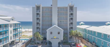 A beachfront hotel with a central building, multiple balconies, and a parking area.
