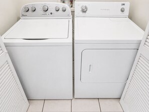 Uma lavanderia com duas secadoras Whirlpool brancas, uma com abertura frontal e outra com abertura superior.