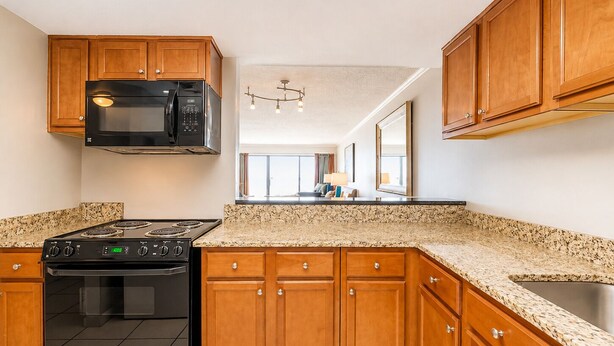 A kitchen with wooden cabinets, a black stove, a microwave, and a granite countertop. - Shoreline Towers (Gulf Shores)