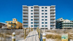 A beachfront hotel with a boardwalk leading to the entrance, surrounded by sand and vegetation. - Shoreline Towers (Gulf Shores)