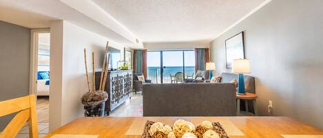 A hotel room with a dining area, a balcony with a view, and a reception desk.