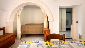 Ein Schlafzimmer mit einem Bett, einem Rundbogenportal, einem Holzstuhl, einem Tisch mit Tischdecke und einem durch das Portal sichtbaren Badezimmer.