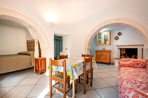 A room with a bed, a dining table with chairs, a sofa, a fireplace, and an arched doorway.