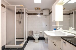 A bathroom with a shower, bidet, sink, and toilet.
