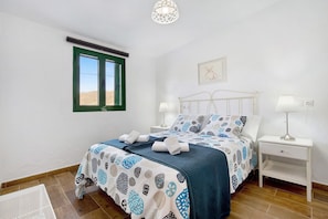 Un dormitorio con cama, mesitas de noche, una ventana y una lámpara en el techo.