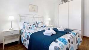 Un letto rifatto con una coperta a fantasia, due lampade da comodino, un comodino e una ventola a parete.