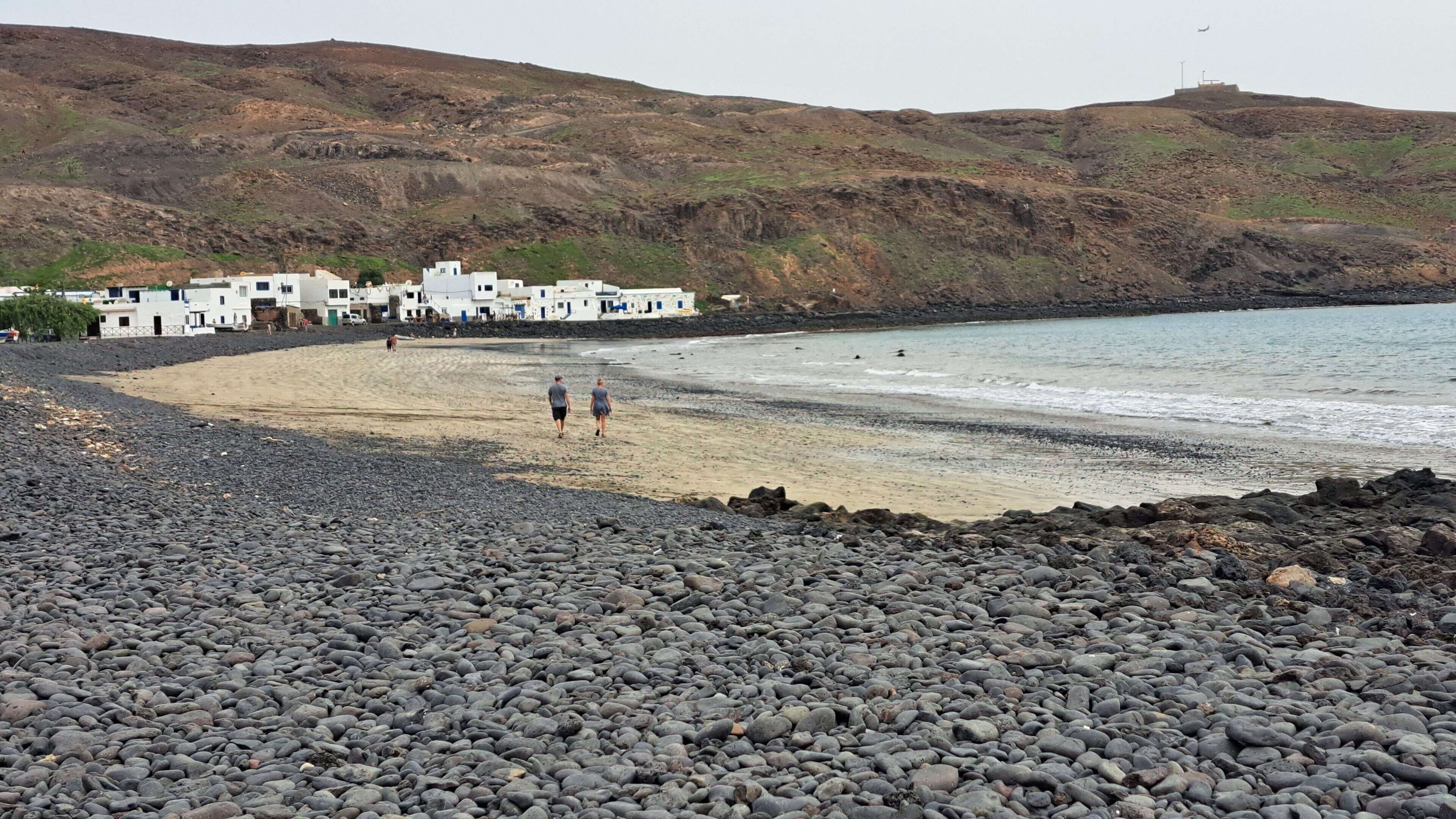 Ein felsiger Strand mit weißen Gebäuden im Hintergrund.