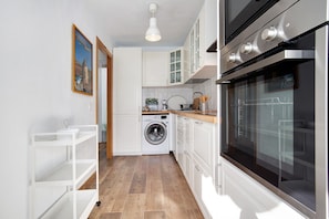 Una cocina compacta con muebles blancos, lavadora y un horno grande.