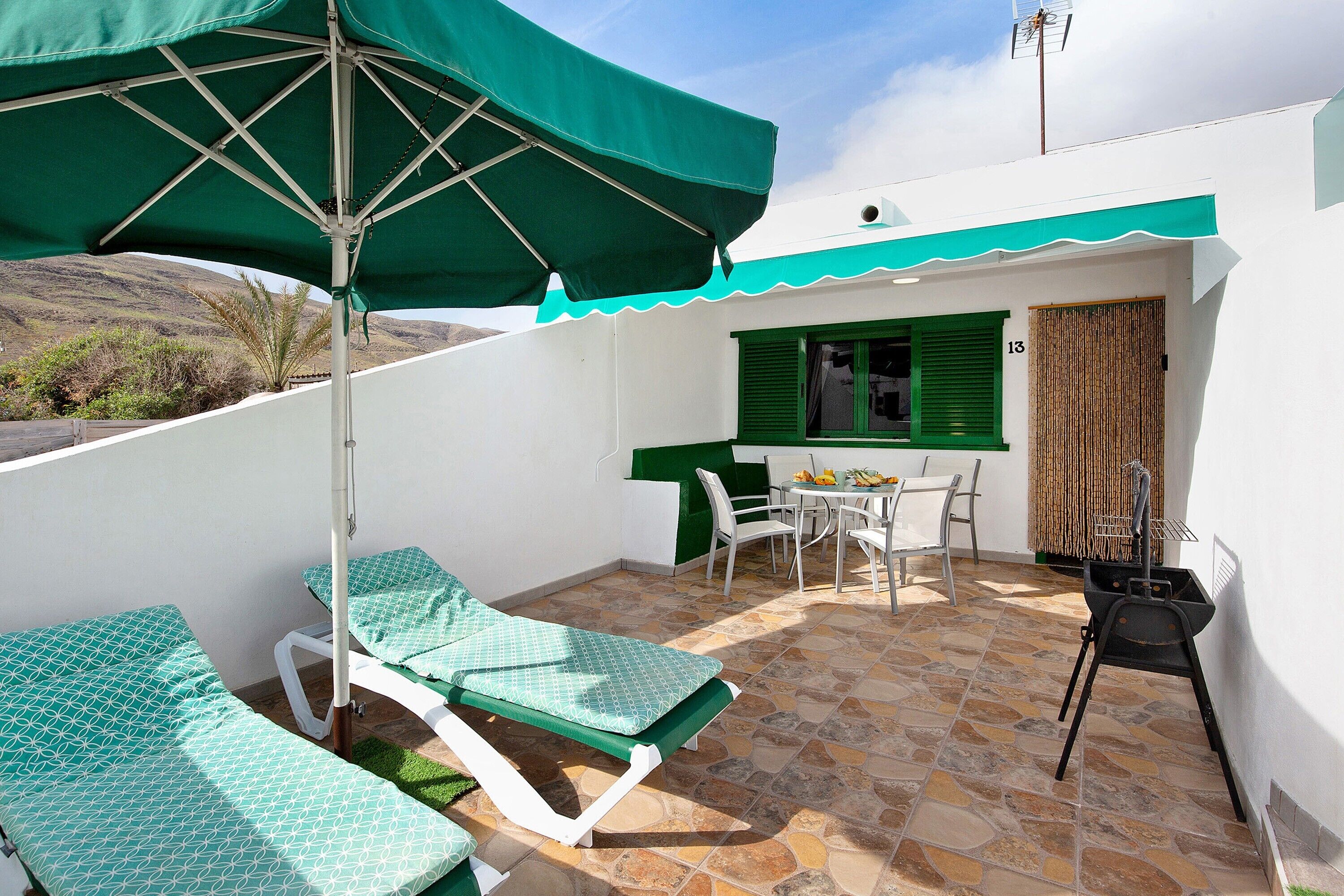 Ein Balkon mit zwei Liegestühlen, einem Tisch mit Stühlen, einem Grill und Blick auf die Hügel.