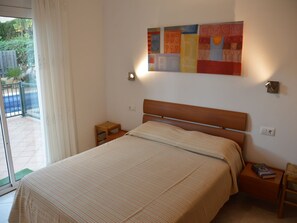 Une chambre à coucher comprenant un lit, une table de chevet, une petite table, une œuvre d’art accrochée au mur et une vue sur l’extérieur grâce à une porte coulissante.
