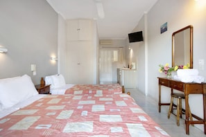 A hotel room with a bed, a desk with a mirror, a dresser, and a bathroom visible in the background.