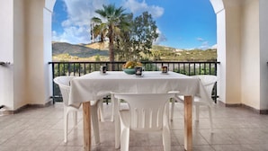 A balcony with a table and chairs, a view of a mountainous landscape, and a palm tree. - Apartment "Dolphin Apartment 1" with Private Balcony, Shared Garden & Wi-Fi (Zakynthos)