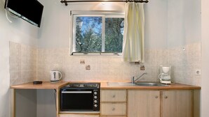 A compact kitchen with a microwave, kettle, and coffee maker, wooden cabinets, a window with a view of trees, and a flat-screen TV mounted on the wall. - Apartment "Dolphin Apartment 1" with Private Balcony, Shared Garden & Wi-Fi (Zakynthos)