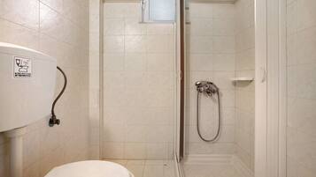 Een kleine badkamer met toilet, douche en raam.