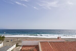 A coastal view with a beach, ocean waves, and a tiled roof.