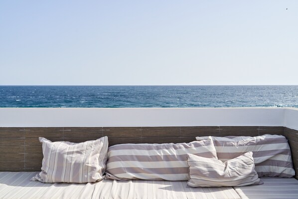 Un balcon avec vue sur la mer, une tête de lit en bois et des coussins à rayures.