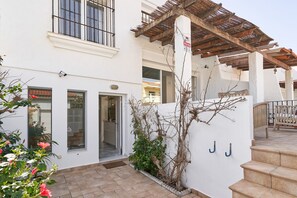 Un bâtiment blanc doté d’une pergola en bois, d’un escalier et d’un petit jardin planté.