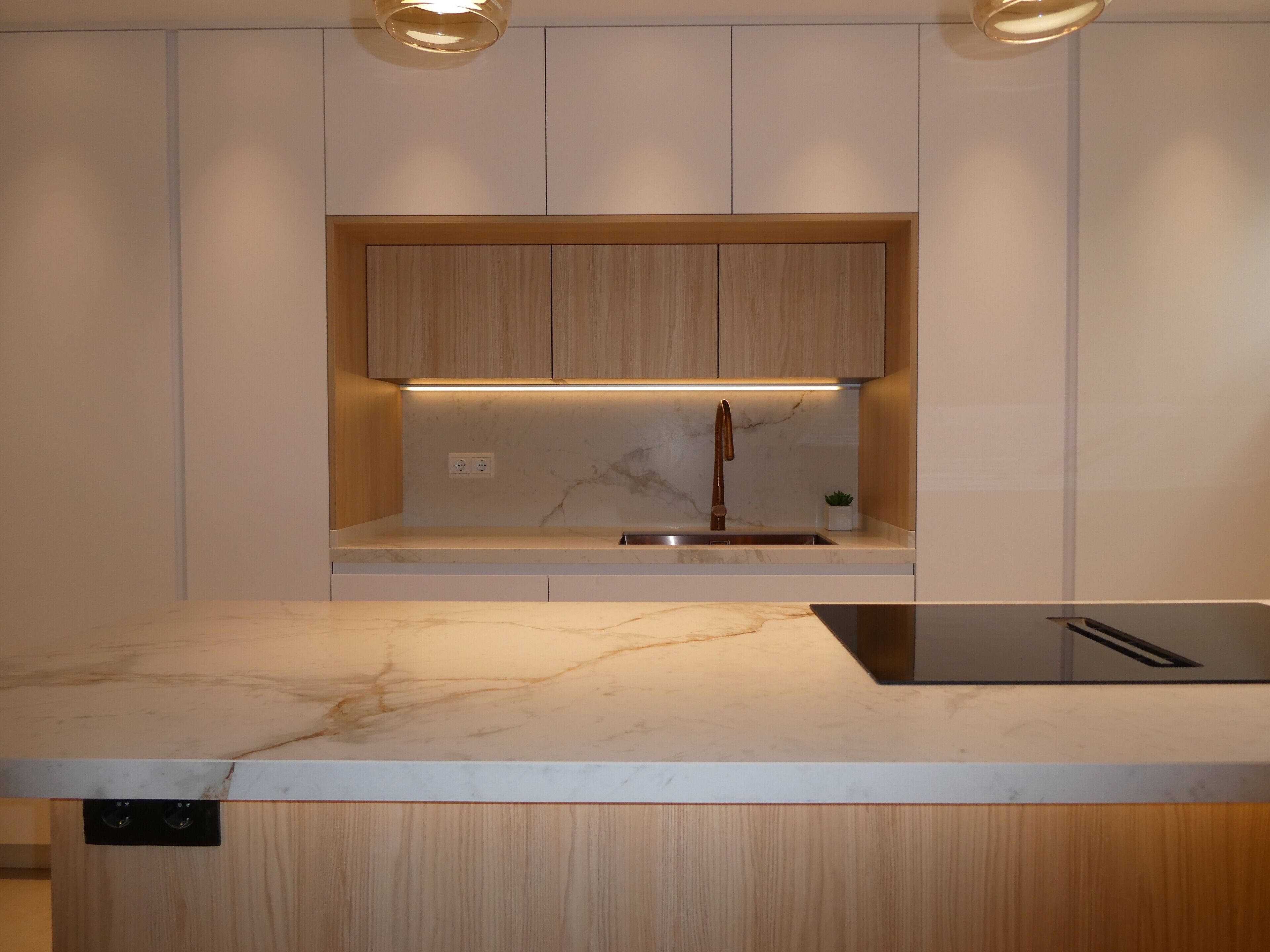 Una cucina moderna con un piano di lavoro in marmo, mobili in legno, lavello incassato e illuminazione sotto pensile.