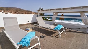 Une terrasse sur le toit avec deux chaises longues, une petite table avec un livre et un verre, et une vue sur l’océan.