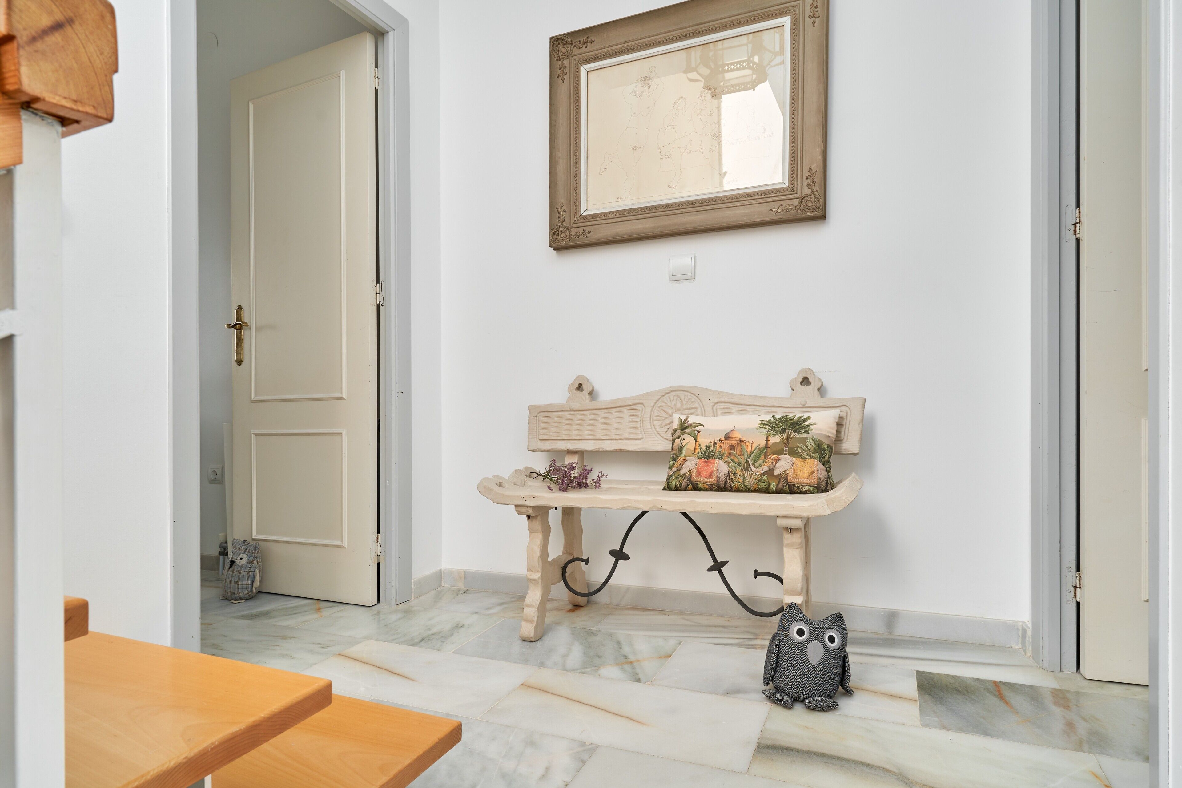Un pasillo con un banco, una puerta, un espejo y una pequeña decoración de lechuzas.