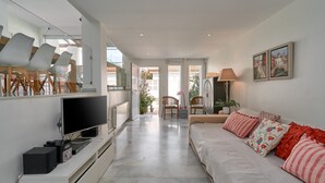 A modern living room with a flat-screen TV, a sofa with patterned cushions, a dining area with chairs, and a view through the glass doors. - Holiday Home "Casa Sueña" Near the Beach with 4 Private Terraces (Calahonda  (Granada))