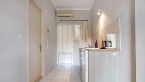 A narrow hallway leading to a kitchen with a washing machine, a coffee maker, and a mirror.