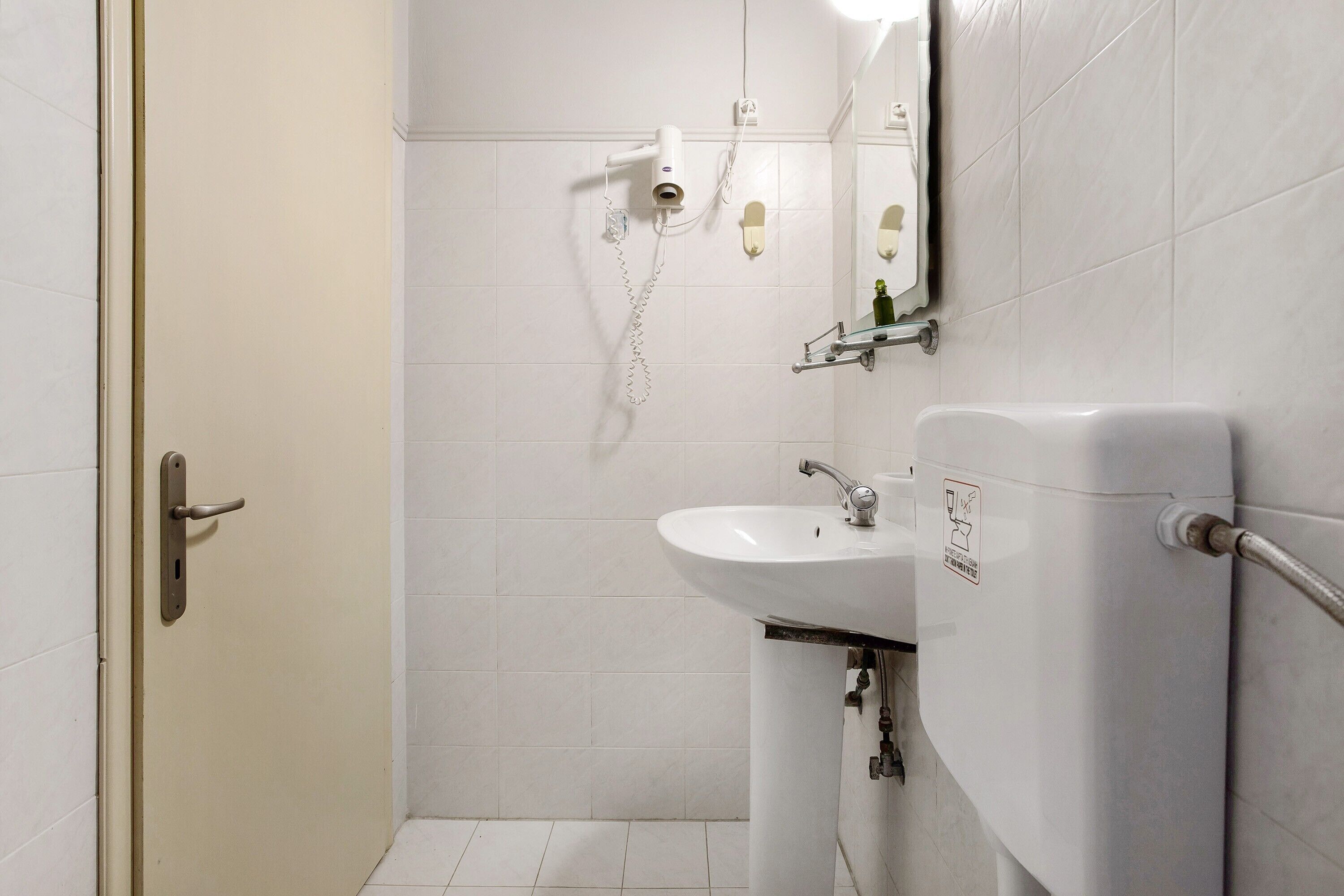 Et badeværelse med en hvid vask, et spejl, en hårtørrer og et toilet.