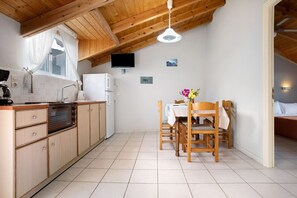 Une cuisine de taille réduite avec des meubles en bois, une table à manger avec des chaises, un téléviseur fixé au mur et un ventilateur de plafond.