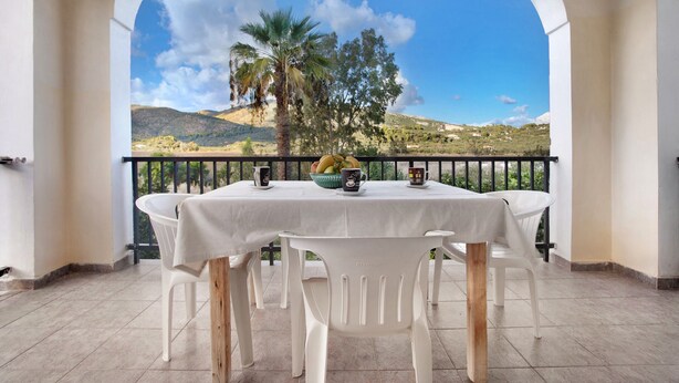 Un balcón con mesa y sillas, vistas a un paisaje montañoso y una palmera.