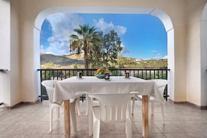 A balcony with a table and chairs, a view of a mountainous landscape, and a palm tree. - Apartment "Dolphin Apartment 8" with Private Balcony, Shared Garden & Wi-Fi (Zakynthos)