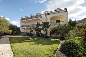 A multi-story building with balconies, a paved pathway, and surrounding greenery. - Apartment "Dolphin Apartment 8" with Private Balcony, Shared Garden & Wi-Fi (Zakynthos)